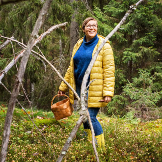 A woman with a basket in her hand stands in a forest.