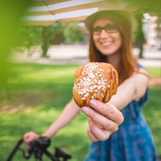 A woman is holding out a cinnamon bun so that it is close to the camera.